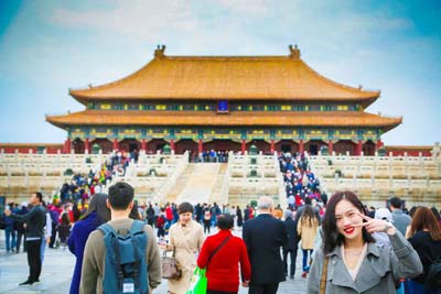 A Chinese woman holding up the peace sign in front of a traditional Chinese building.