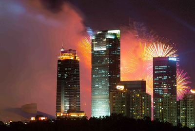 Skyline of Shenzhen China at night with fireworks going off behind the buildings.
