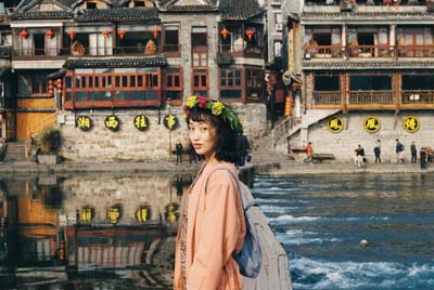 A photo of an Asian woman wearing a floral headband, with a lake and temple in the background